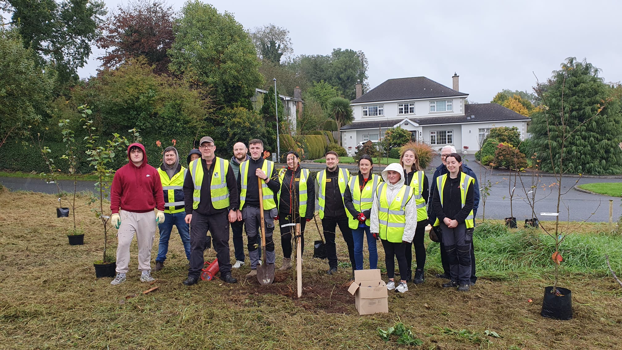 Group of people in hi-vis jackets with young trees they have just planted